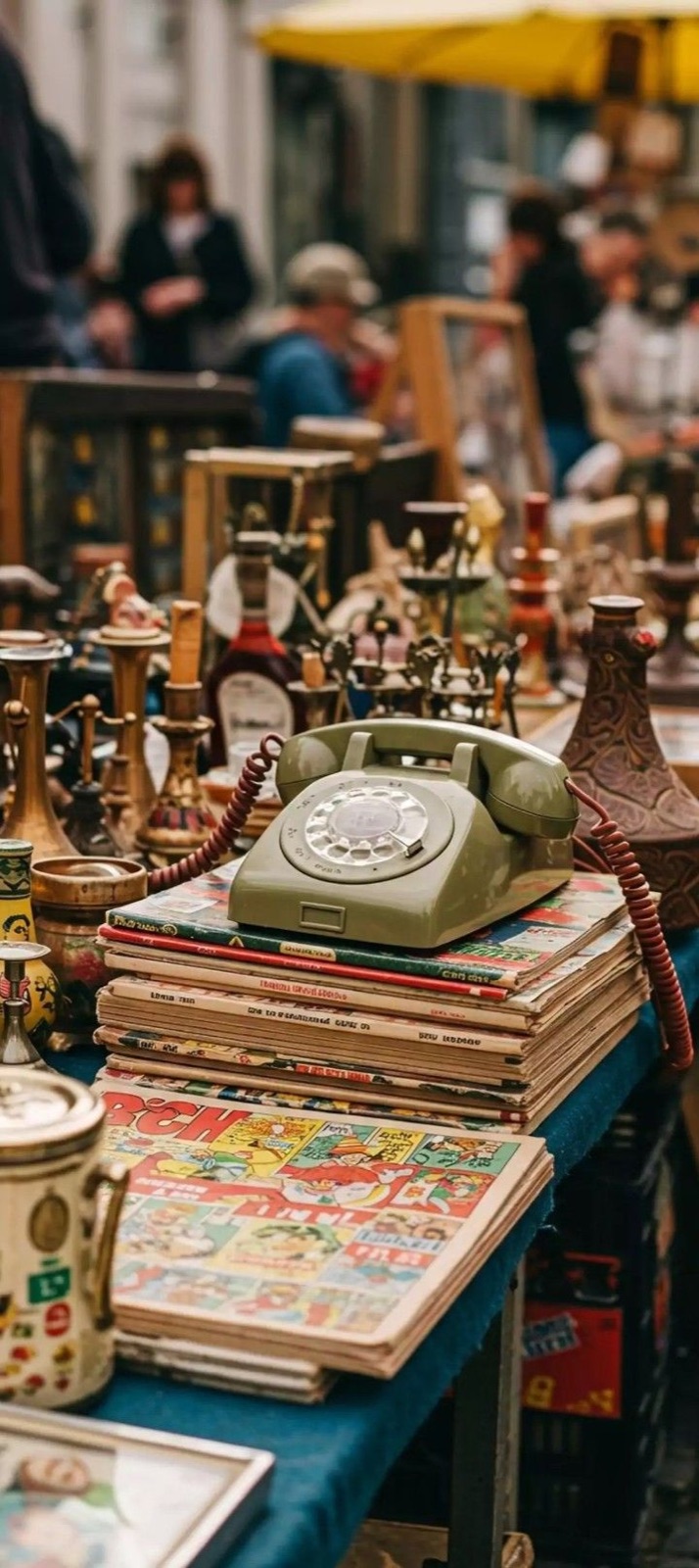 A green rotary phone among books and antiques at a market